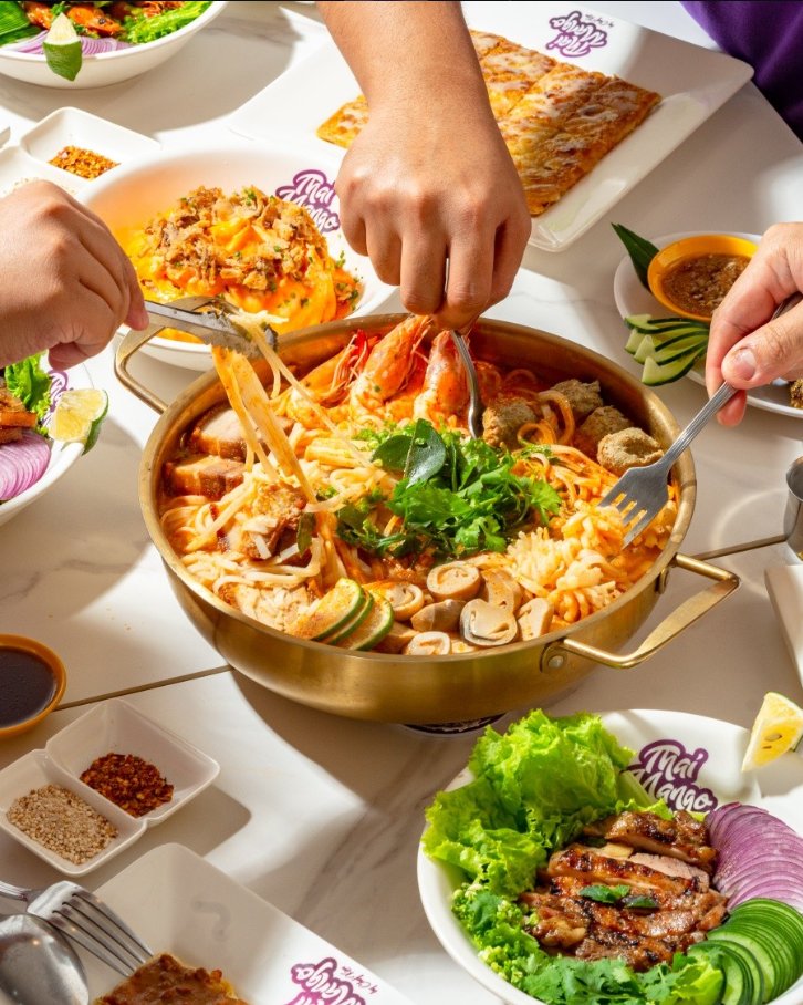 A sharing table with a golden pot of tom yum noodles, grilled pork and other Thai dishes